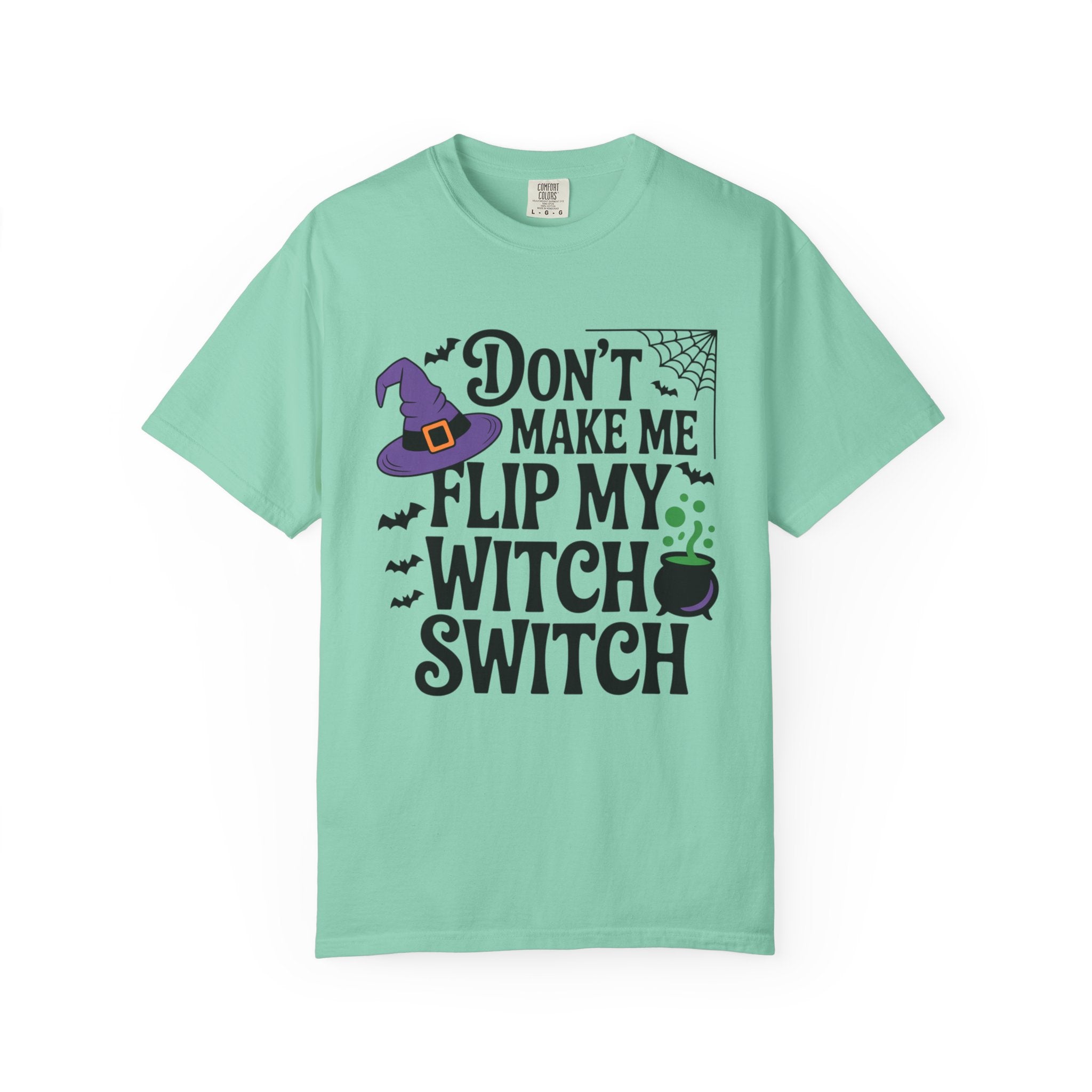A mint green short-sleeve t-shirt with a Halloween graphic that reads 'DON'T MAKE ME FLIP MY WITCH SWITCH' in black text, accompanied by a purple witch hat, black spiderweb, bats, and a green cauldron.