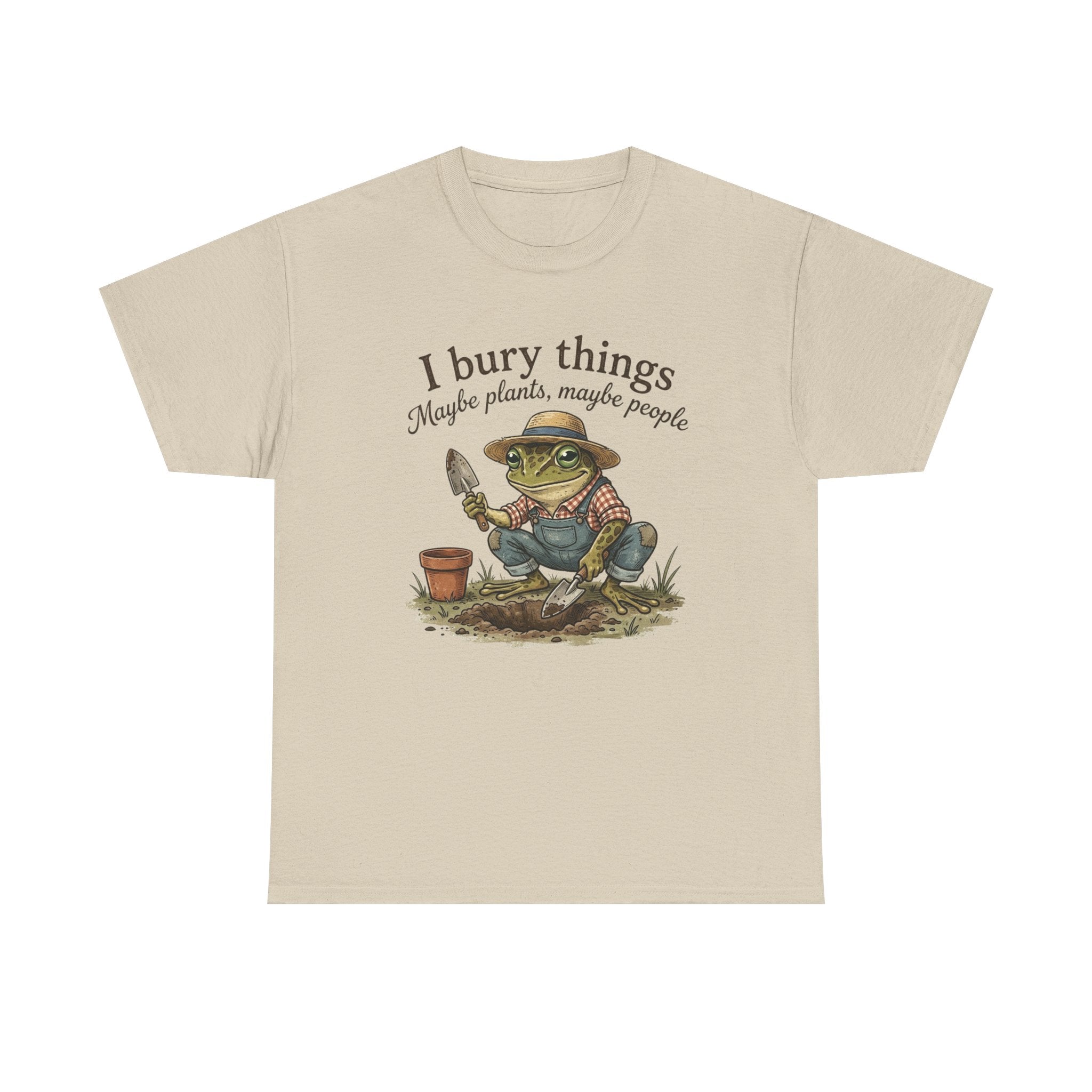 A beige crewneck t-shirt featuring a cartoon graphic of a green frog wearing a straw hat and blue overalls, gardening with a trowel and small pot. Above the graphic, the text reads 'I bury things Maybe plants, maybe people'.