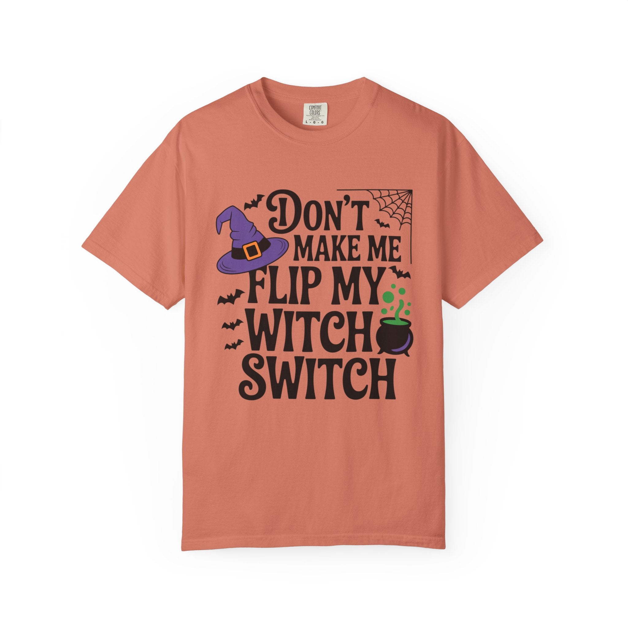 A peach-colored short-sleeve t-shirt with a Halloween graphic that reads 'DON'T MAKE ME FLIP MY WITCH SWITCH' in black text, accompanied by a purple witch hat, black bats, a spiderweb, and a green cauldron.