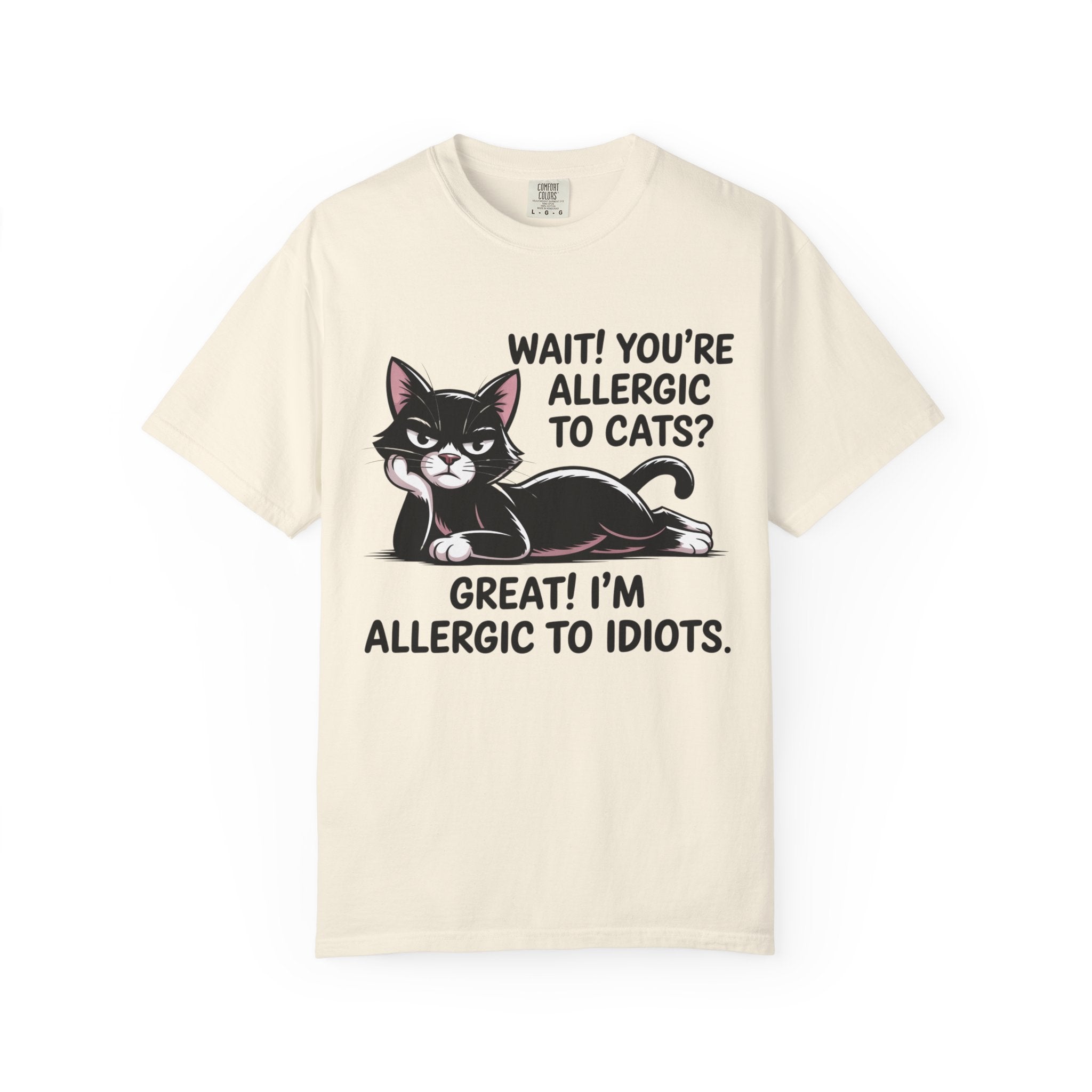 A cream-colored short-sleeve t-shirt with a graphic of a black and white cat lying down, accompanied by the text 'WAIT! YOU'RE ALLERGIC TO CATS? GREAT! I'M ALLERGIC TO IDIOTS.'.