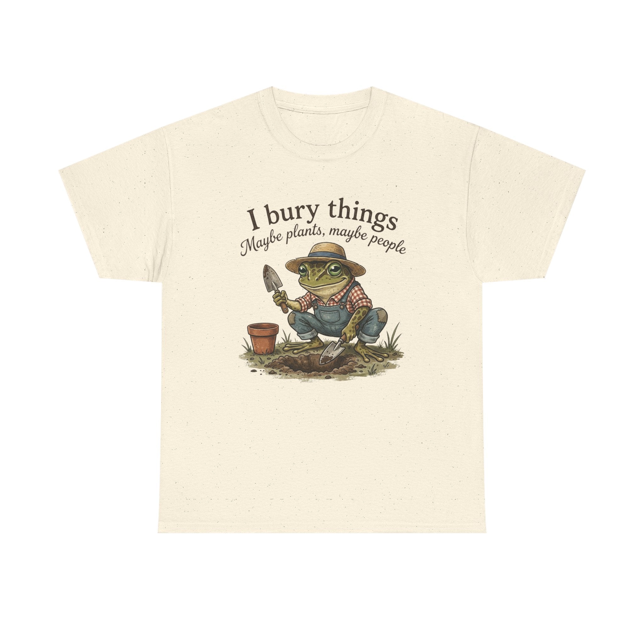 An off-white short-sleeve t-shirt with a graphic of a cartoon frog gardening, accompanied by the text 'I bury things Maybe plants, maybe people'.
