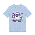 A light blue short-sleeve t-shirt with a cartoon graphic of a ghost wearing sunglasses and making a peace sign, with the text 'STAY WEIRD' below it, on a solid white background.