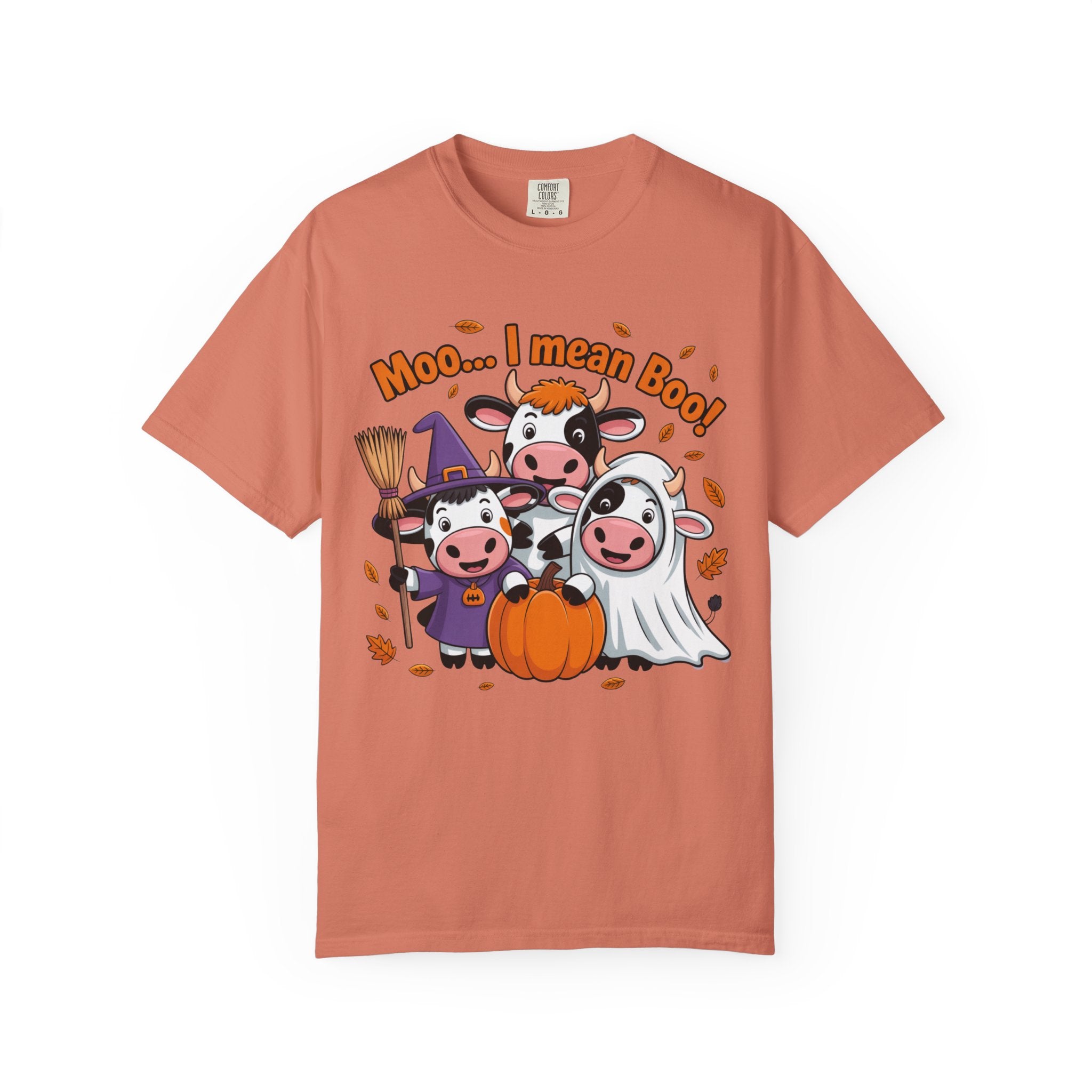 A peach-colored short-sleeve t-shirt with a cartoon graphic of three cows in Halloween costumes (wizard, vampire, and ghost) next to a pumpkin, with the text 'Moo.